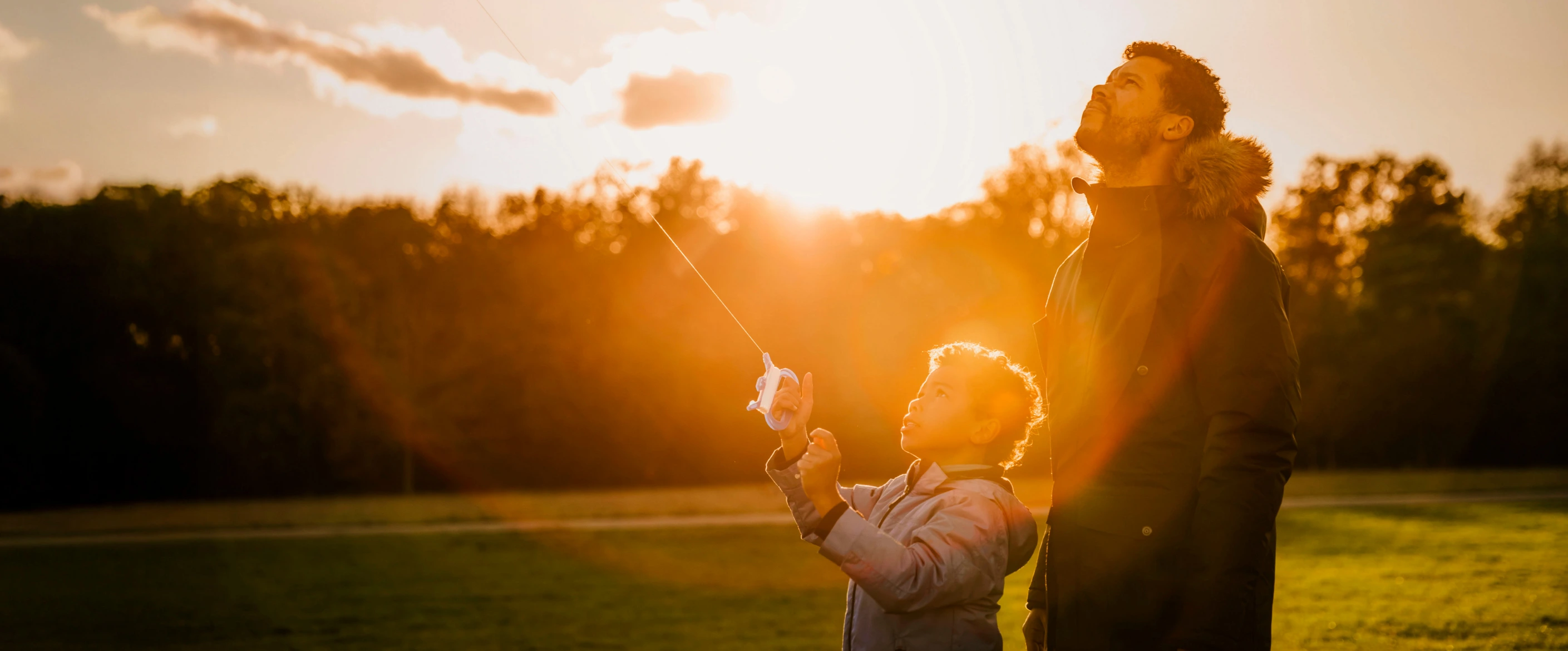 Father and child flying a kite at sunset on a grassy field, sharing a tender outdoor moment